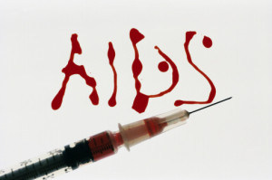 Close-up of AIDS written in blood next to a syringe